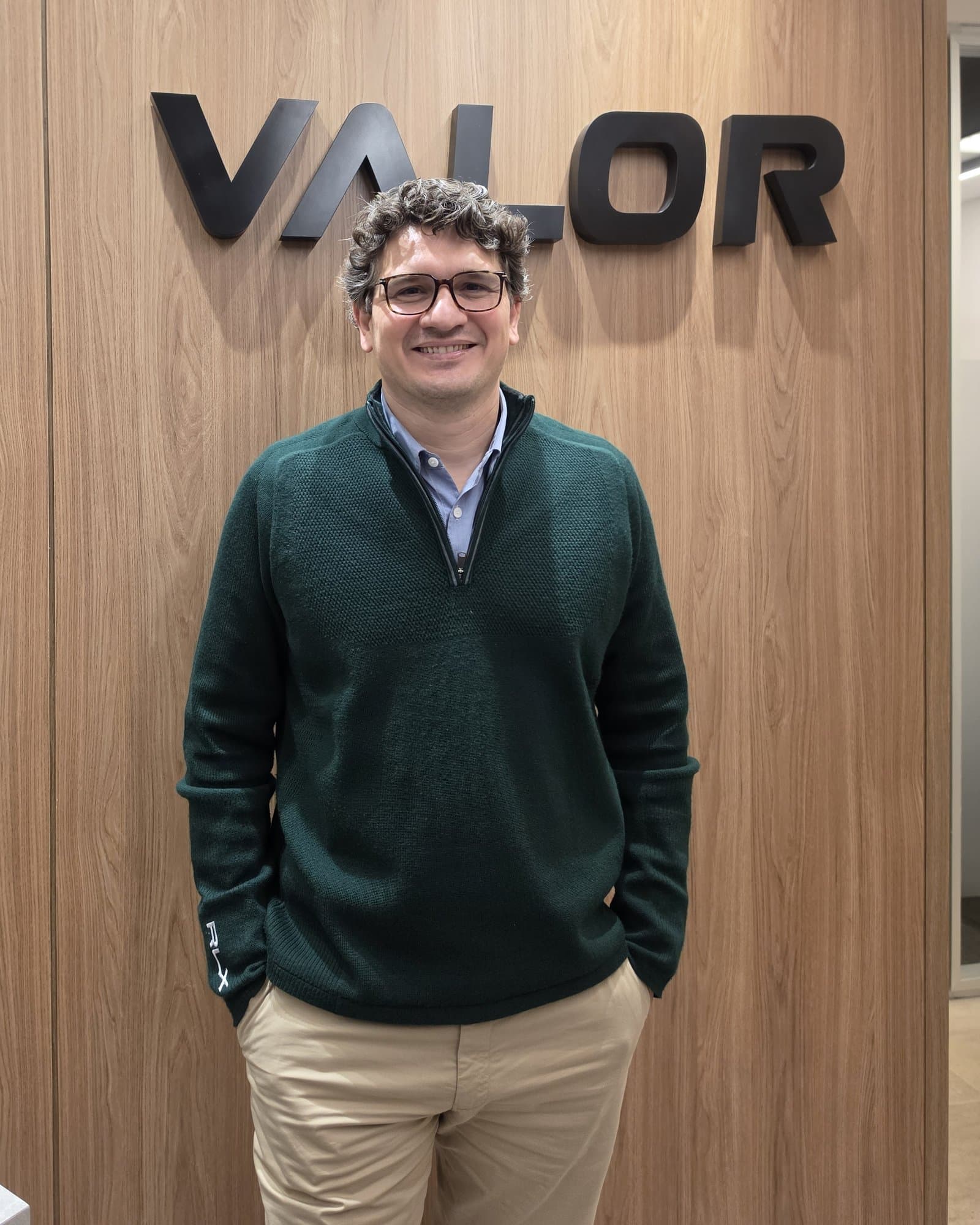 Ramon Serrão Coser, sorrindo, em frente ao letreiro da Valor Investimentos